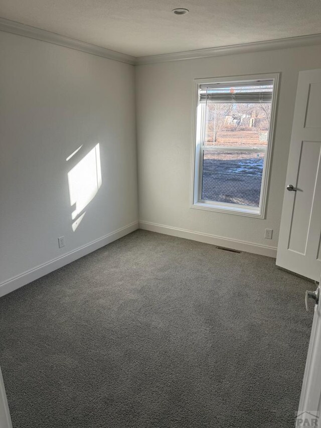 empty room with carpet floors, visible vents, baseboards, and crown molding