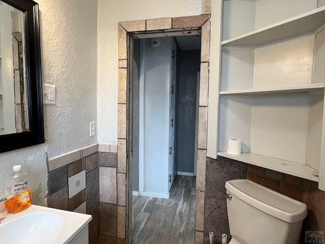 bathroom featuring wood finished floors, a wainscoted wall, tile walls, toilet, and a textured wall