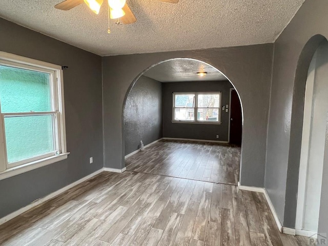 spare room with a ceiling fan, a textured ceiling, wood finished floors, arched walkways, and baseboards