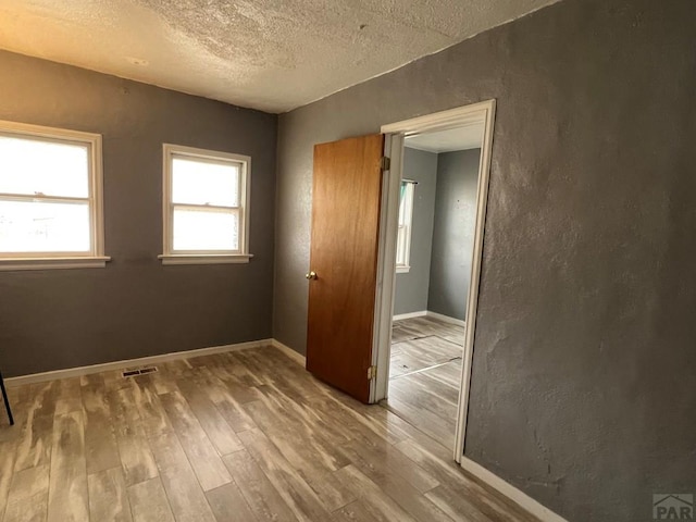 spare room with visible vents, baseboards, a textured ceiling, and wood finished floors