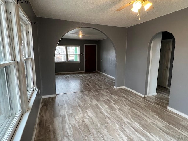 unfurnished room featuring arched walkways, baseboards, a ceiling fan, and wood finished floors