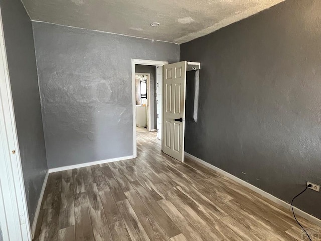 spare room featuring baseboards, wood finished floors, and a textured wall