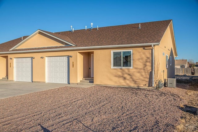 ranch-style home with stucco siding, a shingled roof, central AC unit, a garage, and driveway