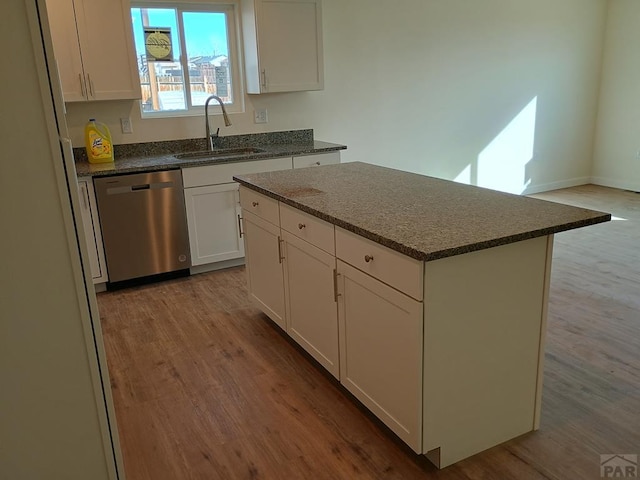 kitchen with wood finished floors, stainless steel dishwasher, a sink, and white cabinetry