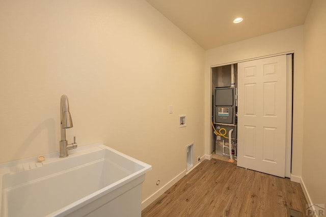 clothes washing area with hookup for a washing machine, a sink, light wood-type flooring, laundry area, and baseboards