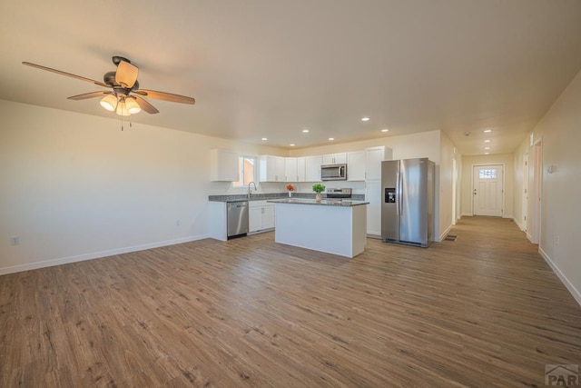 kitchen featuring open floor plan, stainless steel appliances, wood finished floors, and white cabinets