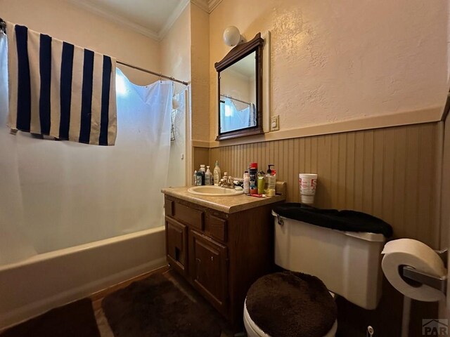 full bathroom with a wainscoted wall, toilet, shower / bath combo with shower curtain, ornamental molding, and vanity