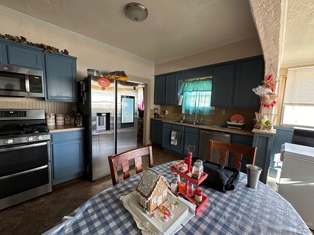 kitchen with light countertops, appliances with stainless steel finishes, ornamental molding, a sink, and dark tile patterned floors