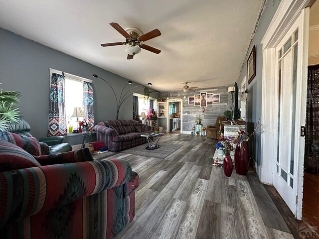 living room with an accent wall, dark wood-style flooring, and a ceiling fan