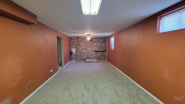 basement with baseboards, visible vents, a ceiling fan, carpet flooring, and a stone fireplace