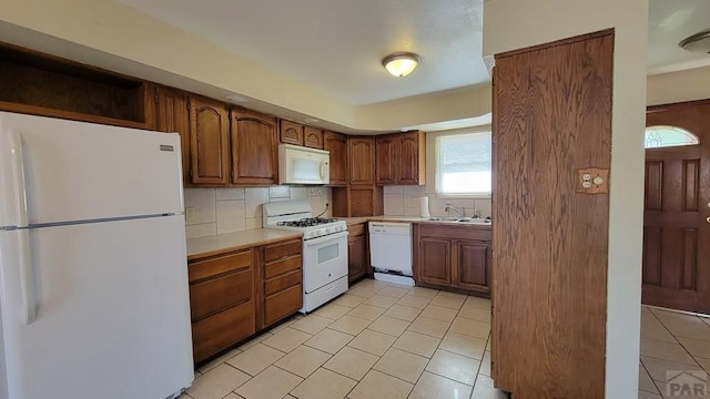 kitchen with brown cabinets, white appliances, light countertops, and a sink