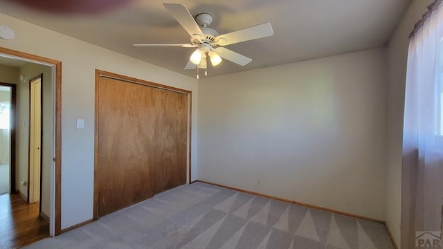 unfurnished bedroom with a closet, carpet, a ceiling fan, and baseboards