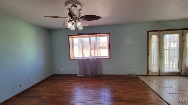 spare room with dark wood-type flooring, visible vents, baseboards, and a ceiling fan