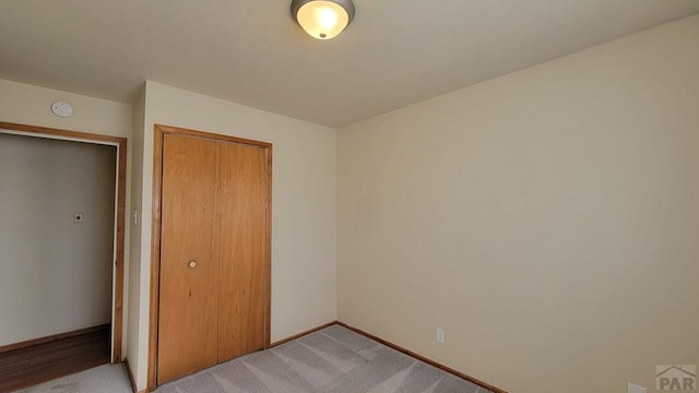 unfurnished bedroom featuring a closet, light colored carpet, and baseboards