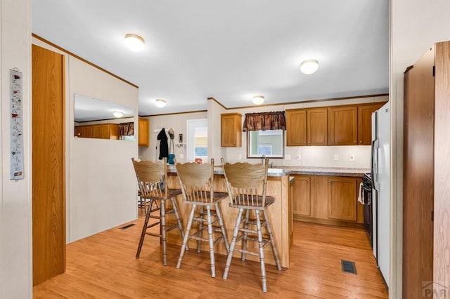 181 6th St, Penrose, CO 81240 - kitchen featuring a breakfast bar, light wood-type flooring, a sink, brown cabinetry, and ornamental molding