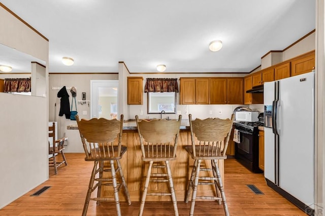 181 6th St, Penrose, CO 81240 - kitchen featuring white appliances, under cabinet range hood, a kitchen bar, light wood-style flooring, and ornamental molding