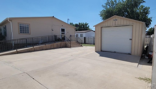 exterior space with a garage, an outbuilding, concrete driveway, and fence