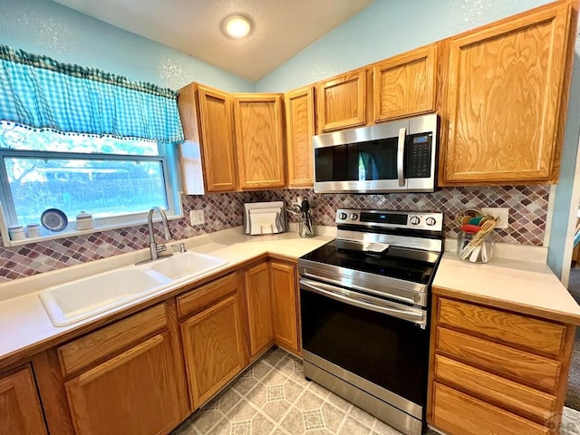 kitchen featuring light countertops, decorative backsplash, appliances with stainless steel finishes, vaulted ceiling, and a sink