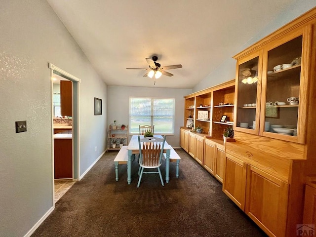 dining room featuring lofted ceiling, baseboards, dark carpet, and a ceiling fan