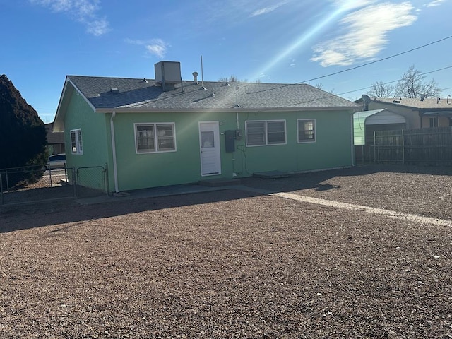 rear view of house with roof with shingles, fence, and stucco siding