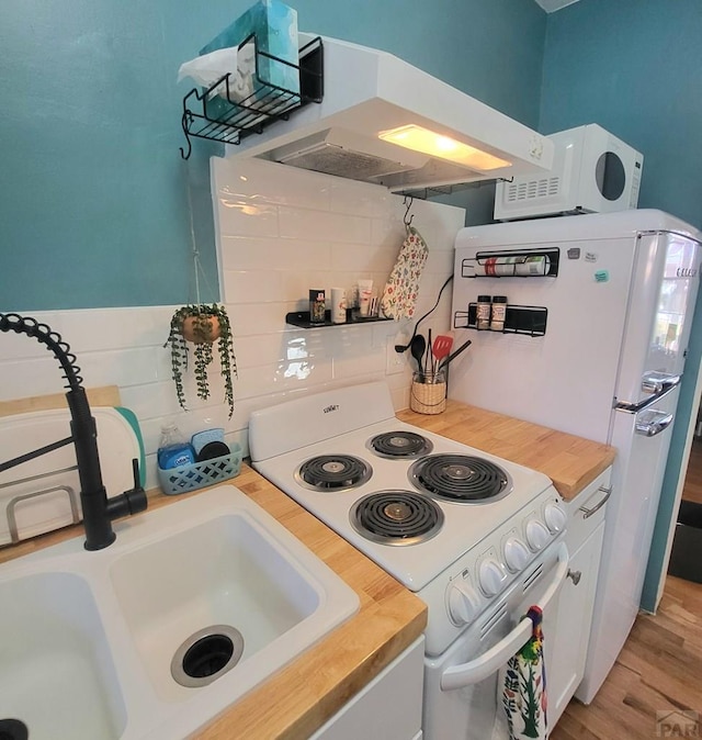 kitchen featuring under cabinet range hood, wood counters, a sink, white appliances, and white cabinets