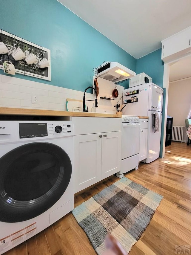 clothes washing area featuring light wood finished floors, laundry area, washer / dryer, and radiator