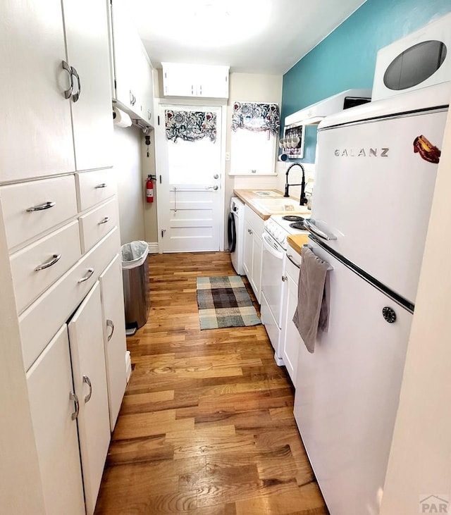 kitchen with light wood finished floors, washer / dryer, white appliances, white cabinetry, and a sink