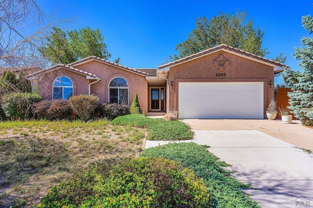 view of front of house with driveway, a tiled roof, an attached garage, and stucco siding