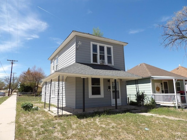 view of front facade featuring covered porch, a shingled roof, and a front lawn