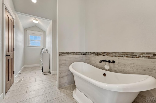 full bathroom with a freestanding tub, lofted ceiling, tile walls, and visible vents