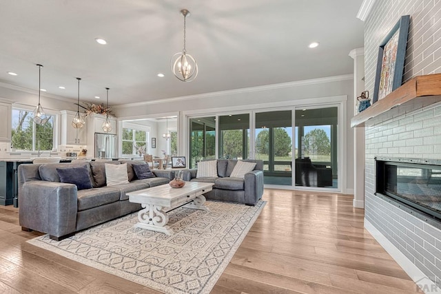 living room with a fireplace, a chandelier, light wood-style floors, and crown molding