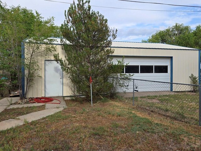 exterior space with an outbuilding, metal roof, a detached garage, fence, and a yard