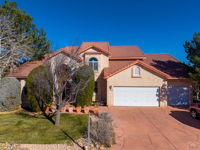 mediterranean / spanish-style house featuring driveway, a tiled roof, an attached garage, a front lawn, and stucco siding