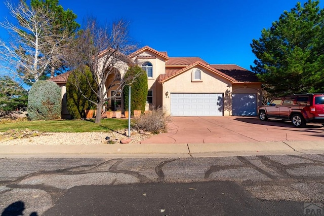 mediterranean / spanish-style home featuring a garage, a tiled roof, driveway, and stucco siding