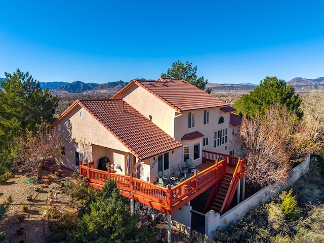 rear view of house featuring a deck with mountain view, a tiled roof, and stairs