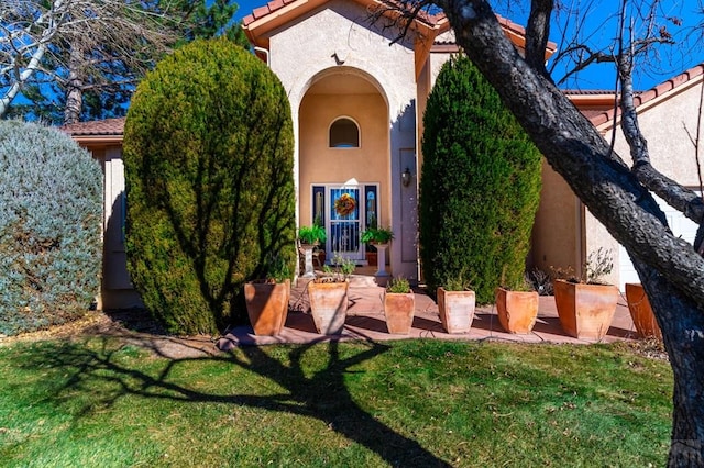 property entrance with a tile roof, a yard, and stucco siding