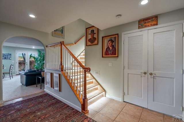 stairway featuring tile patterned floors, baseboards, arched walkways, and recessed lighting