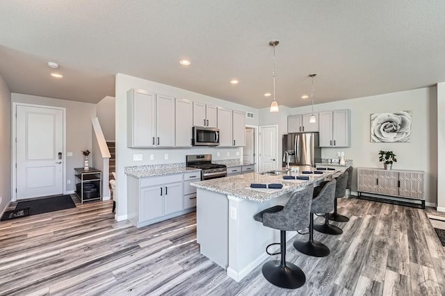 kitchen with light stone counters, hanging light fixtures, appliances with stainless steel finishes, a kitchen island with sink, and a kitchen breakfast bar