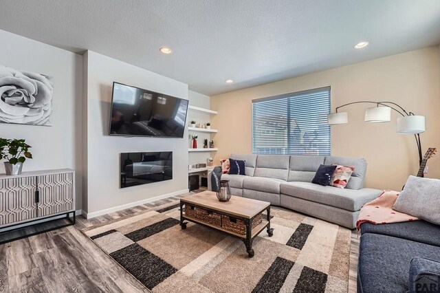 living room featuring a glass covered fireplace, baseboards, recessed lighting, and wood finished floors