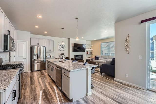 kitchen featuring stainless steel appliances, a kitchen island with sink, a sink, and light stone countertops