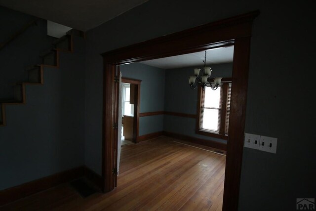 unfurnished dining area featuring baseboards, wood finished floors, and an inviting chandelier