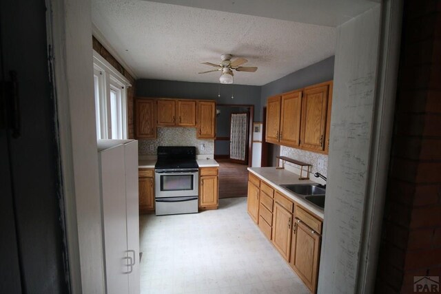 kitchen with light floors, stainless steel electric stove, light countertops, ceiling fan, and a sink