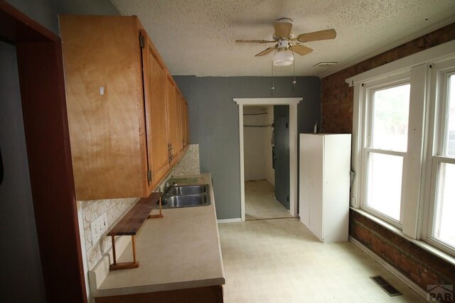 kitchen featuring visible vents, brown cabinetry, light countertops, light floors, and a sink