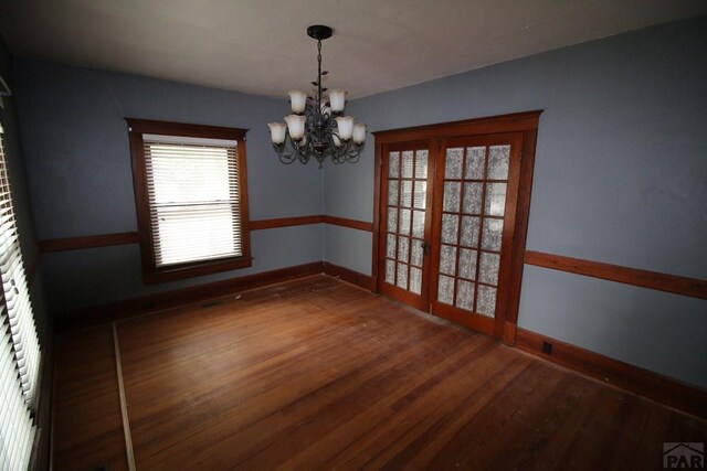 unfurnished dining area with a wealth of natural light, baseboards, a chandelier, and wood finished floors