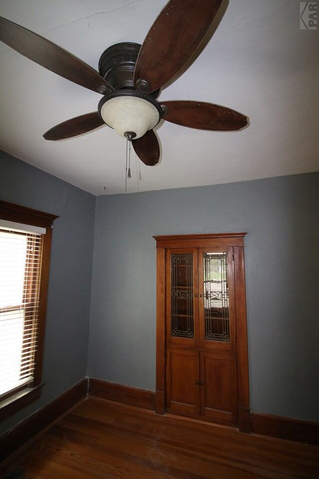 spare room with a ceiling fan, baseboards, and dark wood-type flooring