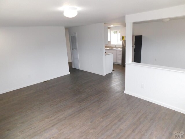 empty room featuring baseboards, dark wood finished floors, and a sink