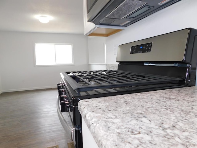 kitchen featuring light stone countertops, stainless steel gas range, baseboards, and dark wood finished floors