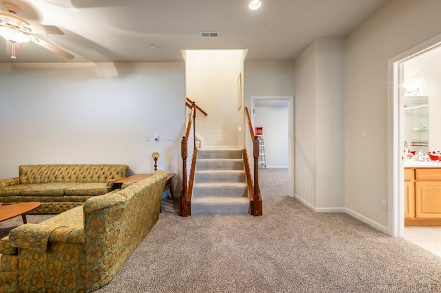 living room with light carpet, visible vents, stairway, and ceiling fan