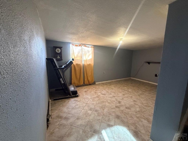 exercise room with a textured wall, a textured ceiling, and baseboards