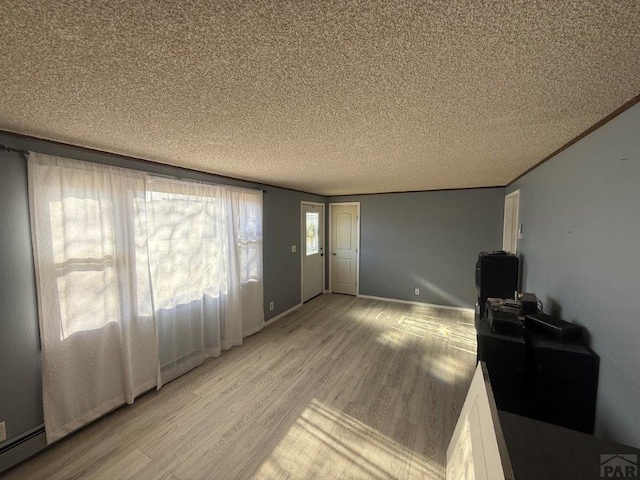 living area featuring a textured ceiling, baseboards, baseboard heating, light wood-type flooring, and crown molding